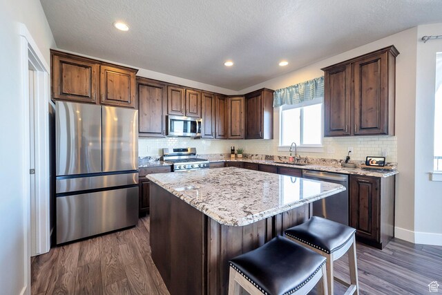4726 W Plainfield Rd S, Herriman, UT 84096 - kitchen with light stone counters, stainless steel appliances, dark wood-type flooring, and a center island