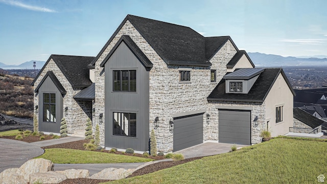 french country style house with a front lawn, metal roof, a garage, stone siding, and a mountain view