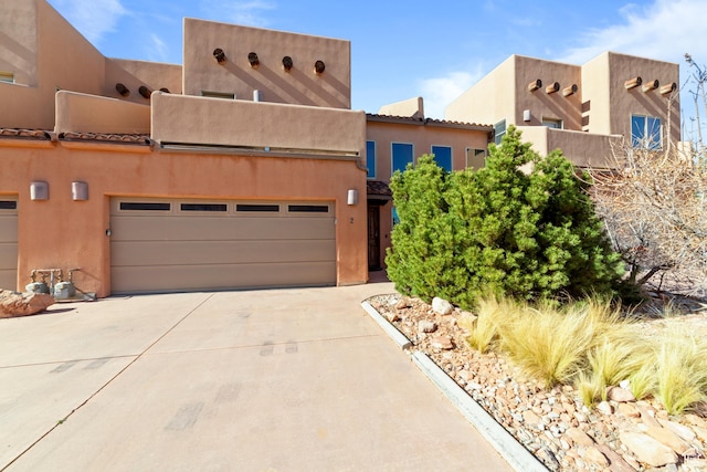 pueblo-style home with a garage, driveway, and stucco siding