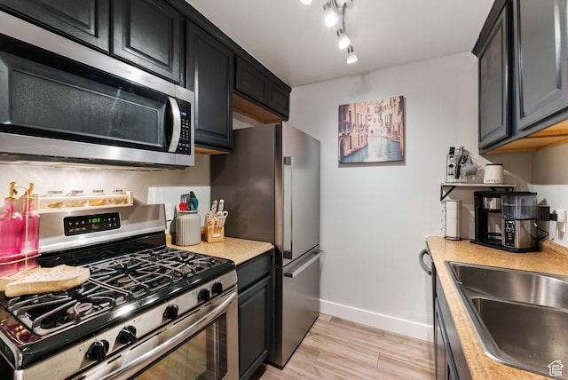 kitchen featuring baseboards, light wood-style flooring, a sink, stainless steel appliances, and light countertops