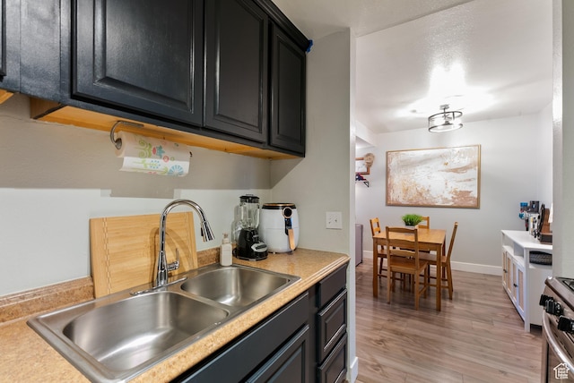 kitchen with light wood finished floors, baseboards, light countertops, gas stove, and a sink
