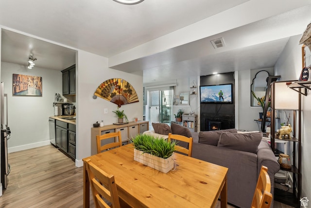 dining space featuring visible vents, light wood-style flooring, baseboards, and a lit fireplace