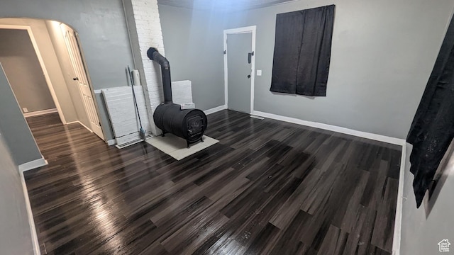 interior space with a wood stove, wood finished floors, arched walkways, and baseboards