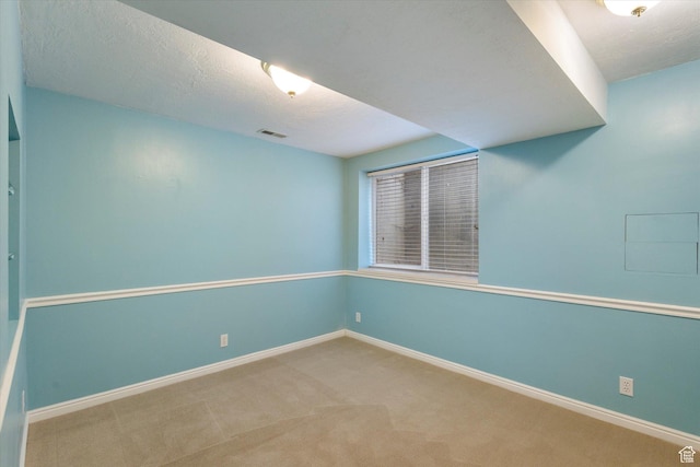 spare room featuring carpet flooring, baseboards, visible vents, and a textured ceiling