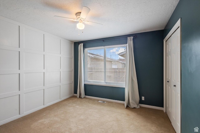 unfurnished bedroom featuring light carpet, a textured ceiling, a closet, a decorative wall, and ceiling fan