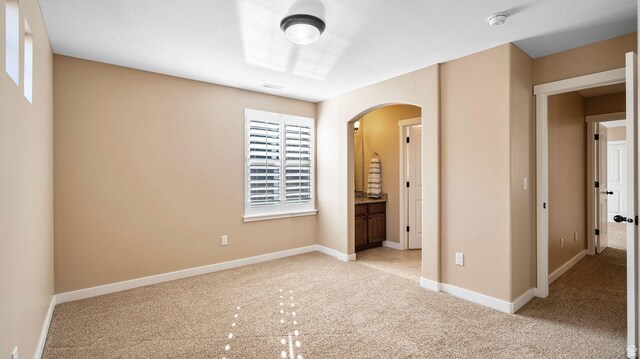 69 W Grove Creek Cir N, Farmington, UT 84025 - unfurnished bedroom featuring arched walkways, light carpet, baseboards, and connected bathroom