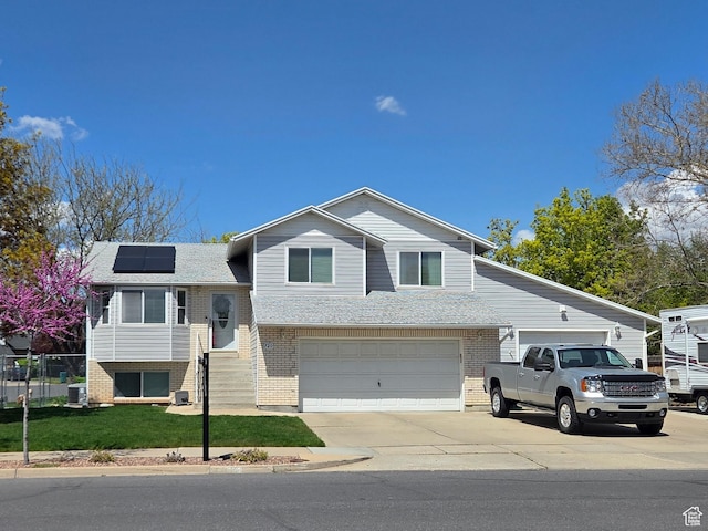 split level home with concrete driveway, a front lawn, an attached garage, solar panels, and brick siding