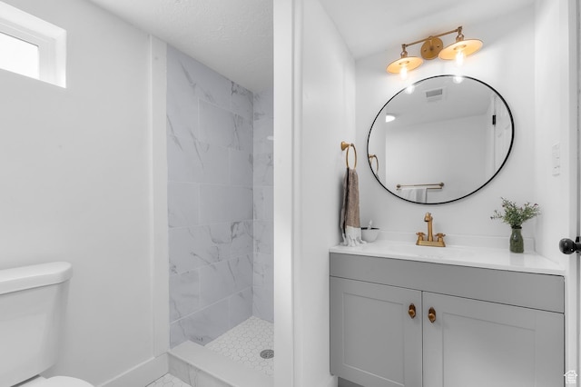full bathroom featuring visible vents, toilet, a tile shower, baseboards, and vanity