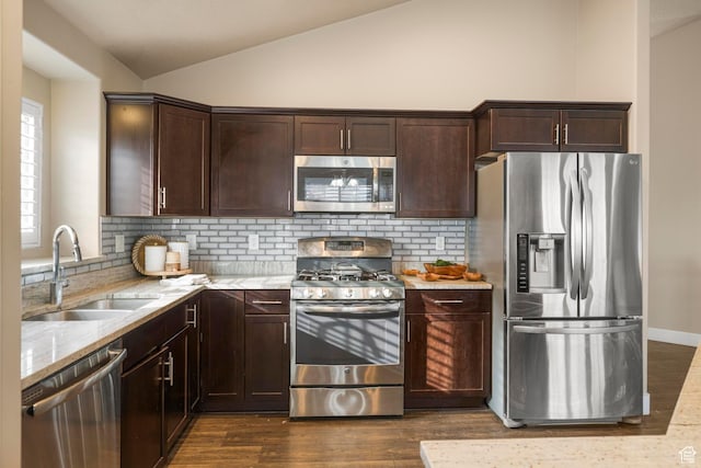 kitchen featuring light stone counters, lofted ceiling, a sink, stainless steel appliances, and dark brown cabinetry
