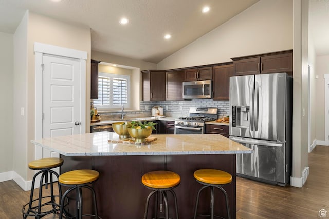 kitchen with a sink, light stone counters, stainless steel appliances, dark brown cabinetry, and lofted ceiling
