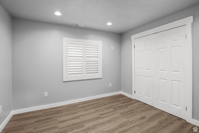 unfurnished bedroom featuring visible vents, a textured ceiling, baseboards, and wood finished floors