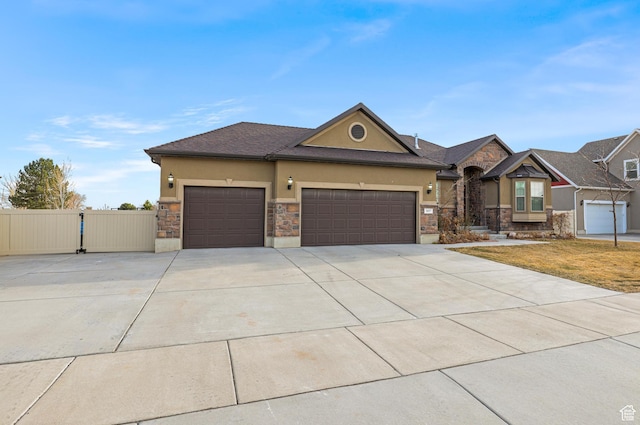 view of front of home with stucco siding, a garage, stone siding, driveway, and a gate