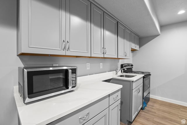 kitchen featuring baseboards, light wood-type flooring, light countertops, appliances with stainless steel finishes, and a textured ceiling