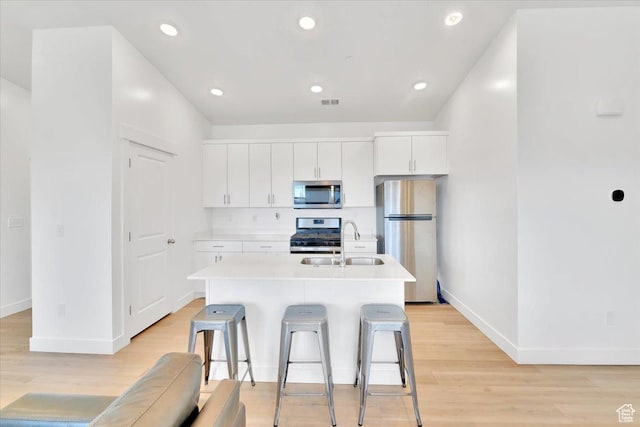 kitchen with a center island with sink, light countertops, light wood-type flooring, appliances with stainless steel finishes, and a sink