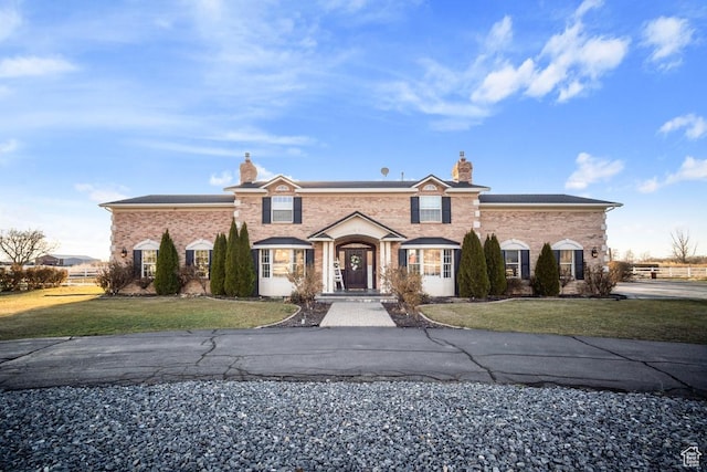 view of front of property featuring brick siding, a chimney, and a front yard