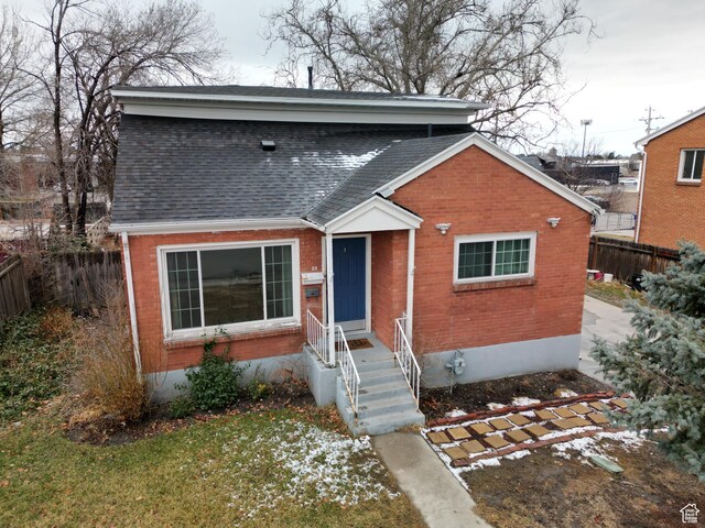 bungalow featuring brick siding, a shingled roof, and fence