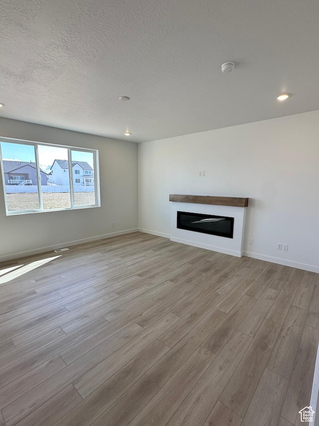 unfurnished living room with a textured ceiling, baseboards, a glass covered fireplace, recessed lighting, and light wood-style flooring