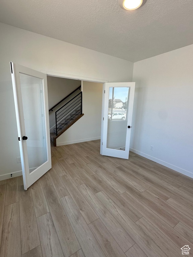 interior space featuring a textured ceiling, baseboards, french doors, and wood finished floors