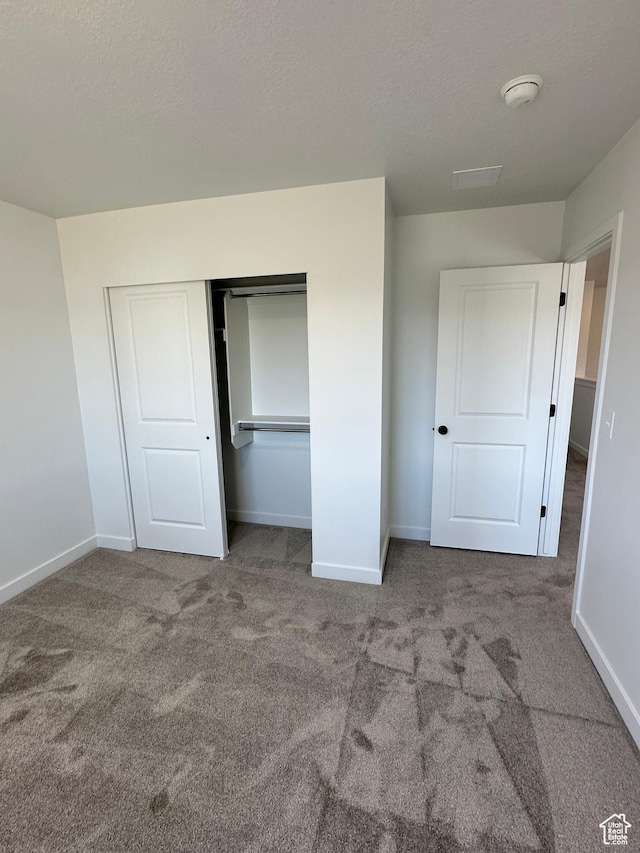 unfurnished bedroom with carpet floors, a textured ceiling, baseboards, and a closet