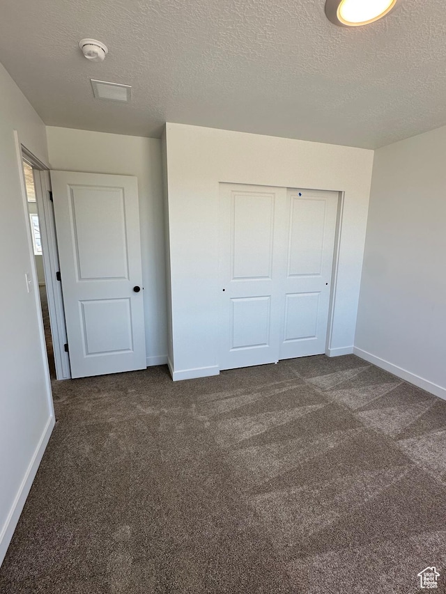 unfurnished bedroom featuring baseboards, a textured ceiling, a closet, and dark colored carpet