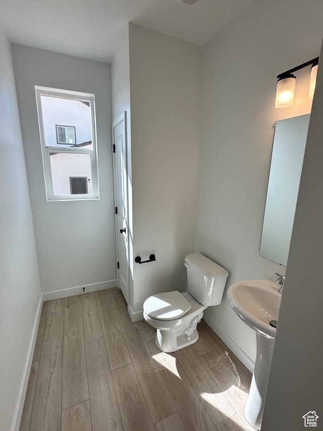 half bathroom with toilet, baseboards, and wood finished floors