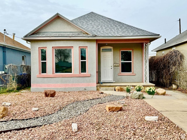 bungalow featuring stucco siding, a porch, fence, and roof with shingles