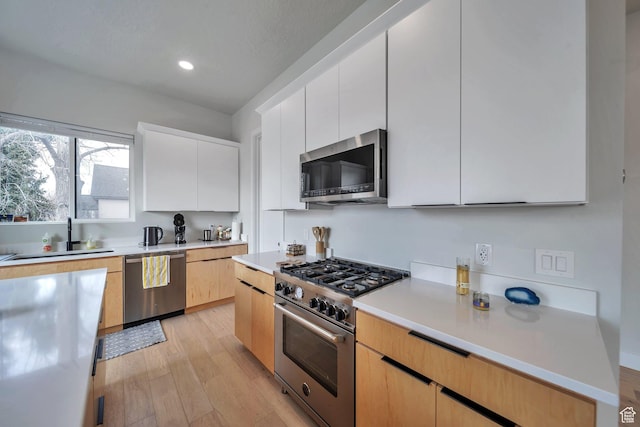 869 S Washington St Unit 101, Salt Lake City, UT 84101 - kitchen with light wood-style flooring, a sink, light countertops, appliances with stainless steel finishes, and white cabinetry