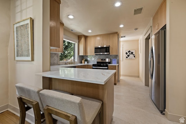 1444 E Sherman Ave, Salt Lake City, UT 84105 - kitchen with backsplash, light stone countertops, a peninsula, stainless steel appliances, and visible vents