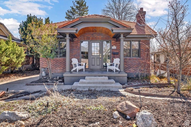 view of front of property with covered porch, a tiled roof, brick siding, and a chimney