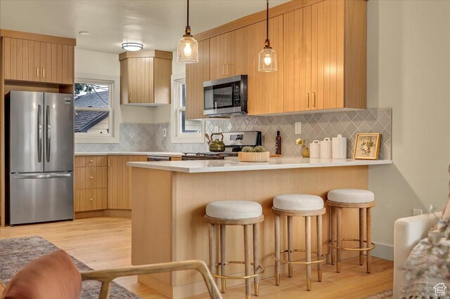 1662 E Browning Ave, Salt Lake City, UT 84105 - kitchen with light wood finished floors, a breakfast bar, appliances with stainless steel finishes, a peninsula, and light countertops