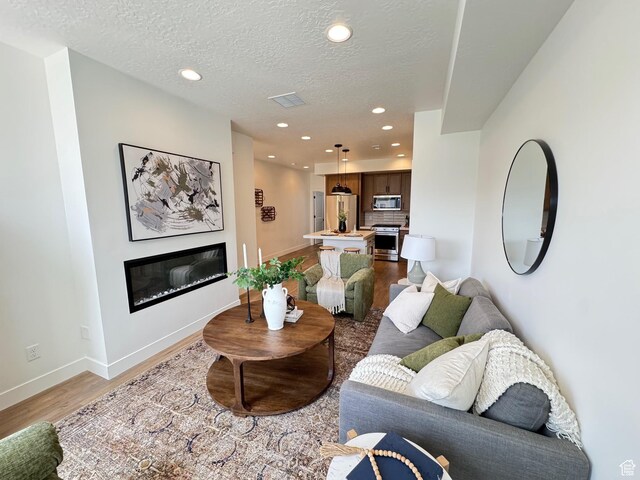 1151 Gambel Oak Way Unit 54, Park City, UT 84098 - living area with a glass covered fireplace, light wood-style flooring, baseboards, recessed lighting, and a textured ceiling