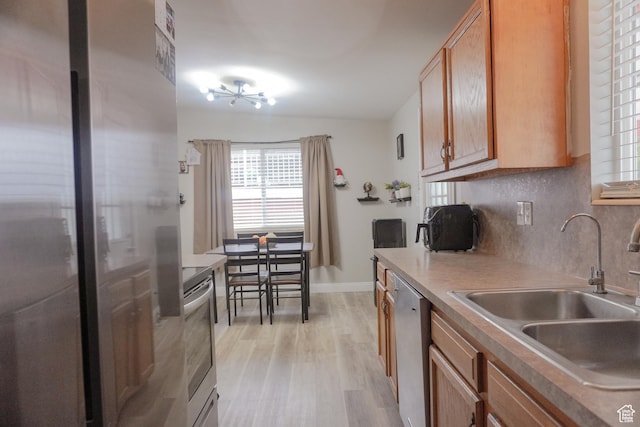1993 W 4200 S, Roy, UT 84067 - kitchen featuring brown cabinetry, light wood-style flooring, stainless steel appliances, a sink, and tasteful backsplash