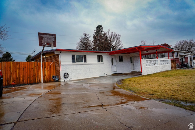 ranch-style home featuring driveway, fence, a front yard, an attached carport, and concrete block siding