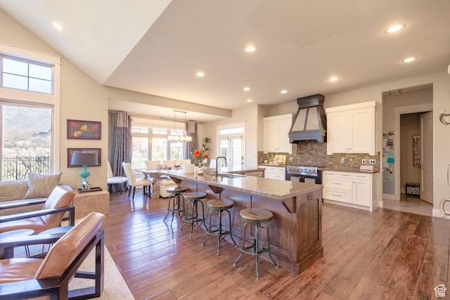 kitchen featuring tasteful backsplash, premium range hood, a breakfast bar area, hardwood / wood-style flooring, and a sink