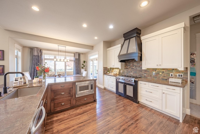 kitchen with light wood-type flooring, custom range hood, a sink, appliances with stainless steel finishes, and decorative backsplash