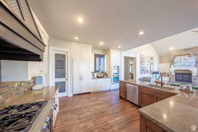 kitchen with a sink, appliances with stainless steel finishes, a fireplace, dark wood-style flooring, and vaulted ceiling