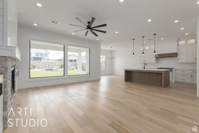3823 S Kennedy Ln, Washington, UT 84780 - unfurnished living room featuring light wood-type flooring, visible vents, ceiling fan with notable chandelier, a sink, and a stone fireplace