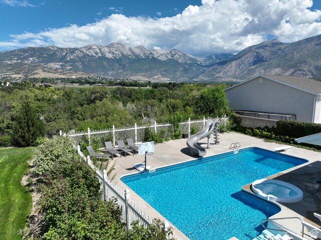 5798 W 11350 N, Highland, UT 84003 - view of swimming pool featuring a pool with connected hot tub, a water slide, a patio, fence, and a mountain view