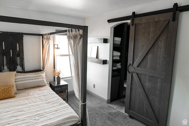 carpeted bedroom featuring a barn door and baseboards
