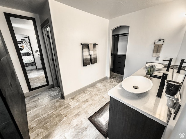 full bathroom with baseboards, double vanity, ensuite bathroom, wood finished floors, and a sink
