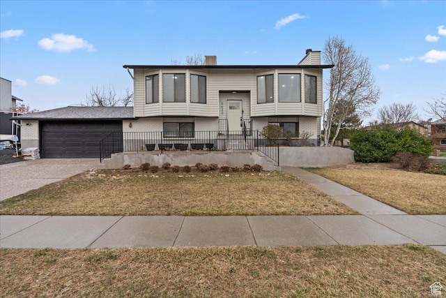 bi-level home with a front yard, an attached garage, a chimney, concrete driveway, and brick siding