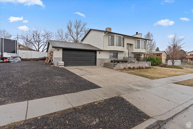 split foyer home featuring brick siding, fence, a chimney, a garage, and driveway