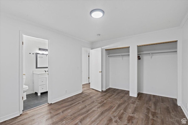 unfurnished bedroom with wood finished floors, baseboards, ensuite bathroom, crown molding, and two closets