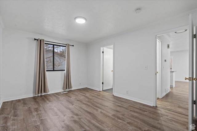 empty room featuring visible vents, crown molding, baseboards, and wood finished floors