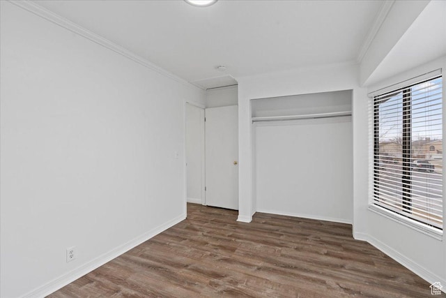 unfurnished bedroom with wood finished floors, a closet, crown molding, baseboards, and attic access