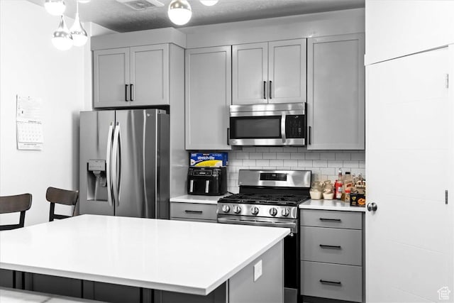 kitchen featuring backsplash, gray cabinetry, a kitchen island, light countertops, and stainless steel appliances