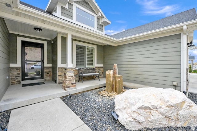 doorway to property with stone siding, a porch, and a shingled roof