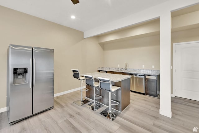 kitchen featuring light wood-style flooring, a kitchen island, appliances with stainless steel finishes, and a breakfast bar area