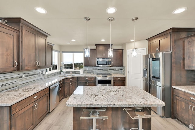kitchen featuring a kitchen island, dark brown cabinetry, decorative backsplash, appliances with stainless steel finishes, and a sink