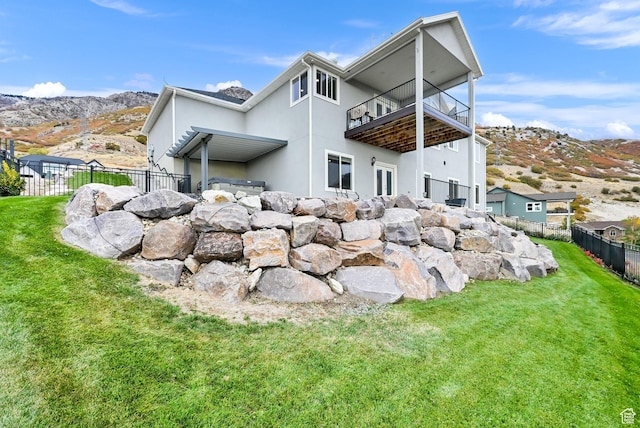 back of house featuring a balcony, a yard, fence, and stucco siding